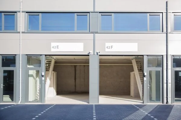 Twee lege bedrijfsunits aan de Laan van s-Gravenmade met open garagedeuren en bovenliggende ramen, genummerd 42E en 42F.